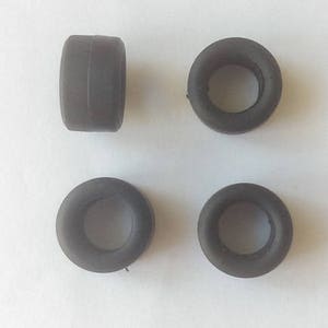 Op de afbeelding: Vier zwarte rubberen banden met een gat in het midden. De banden zijn ongeveer 2,5 cm in diameter.