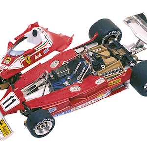 Peut inclure: Modèle réduit rouge d'une Ferrari de Formule 1, portant le numéro 11. Il est équipé de pneus noirs Goodyear, d'un aileron arrière blanc et d'autocollants de sponsors. La carrosserie est partiellement démontée.