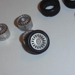 Könnte beinhalten: Eine Sammlung von Modellauto-Rädern. Die Räder haben ein silberfarbenes Mehrspeichen-Design und sind mit schwarzen Gummireifen kombiniert. Einige Räder sind von den Reifen getrennt. Die Räder sind wahrscheinlich für ein Modellauto oder ein ähnliches Projekt.