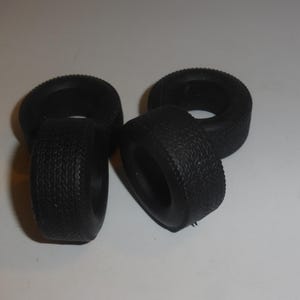 Può includere: Quattro pneumatici in gomma nera con fianchi strutturati. I pneumatici sono disposti in gruppo, con due in posizione verticale e due sdraiati su un lato. I pneumatici sembrano essere per un piccolo veicolo o modello.