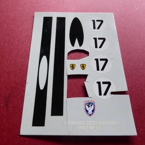 Peut inclure: Une feuille d'autocollants pour un modèle Ferrari Testarossa. Les décalcomanies sont gris clair avec des rayures noires, le numéro 17 dans des cercles blancs et des logos Ferrari. Le texte en bas indique "FERRARI TESTAROSSA 1957 N 17".