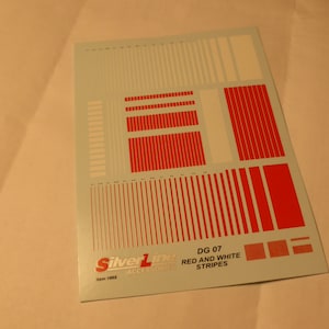 Può includere: Un foglio di decalcomanie a strisce rosse e bianche per la decorazione di modelli di auto. Il foglio è etichettato "DG 07 Red and White Stripes" e "Silverline Accessories Item 1902".