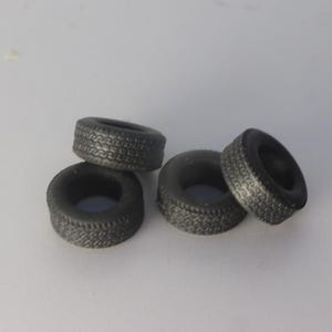 Può includere: Quattro piccoli pneumatici in gomma nera con dettagliati motivi del battistrada. I pneumatici sono disposti in un gruppo allentato, alcuni impilati l'uno sull'altro. I pneumatici sembrano essere per un'auto modello o un piccolo veicolo simile.