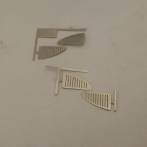 Puede incluir: Cuatro piezas de metal con un patrón de rejilla decorativo. Las piezas están diseñadas para ser utilizadas como rejillas de ventanas para un tren modelo.