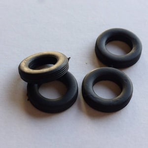 Könnte beinhalten: Vier schwarze Gummireifen für ein Spielzeugauto oder Modell. Die Reifen haben einen Durchmesser von etwa 2,5 cm.