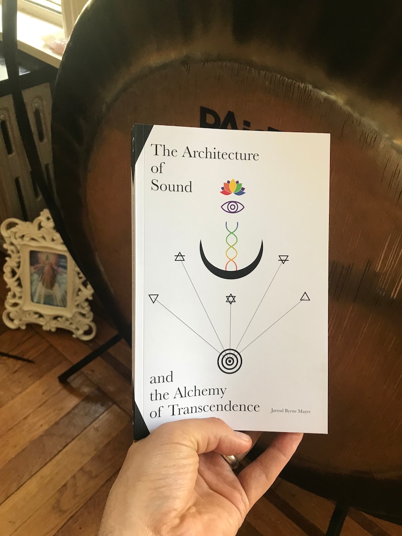 Puede incluir: Un libro blanco con el t&iacute;tulo "The Architecture of Sound and the Alchemy of Transcendence" de Jarrod Byrne Mayer. La portada presenta una ilustraci&oacute;n en blanco y negro de una luna creciente, una estrella, un c&iacute;rculo y una flor de loto.