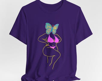 Puede incluir: Camiseta morada con un diseño gráfico. El diseño presenta una persona en bikini rosa con una mariposa en lugar de una cabeza. La mariposa tiene alas azules, amarillas y verdes, y el contorno es amarillo.