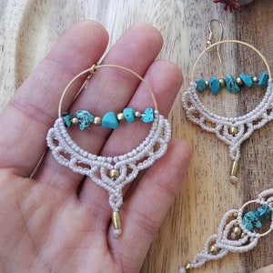 May include: A handmade jewelry set featuring macrame earrings and a bracelet. The earrings have gold hoops with turquoise stones and a cream-colored macrame design. The bracelet also has turquoise stones and gold beads. The set is displayed on a wooden surface.