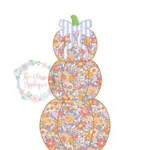 May include: A stack of three pumpkins with a floral pattern and a blue and white striped bow on top. The pumpkins are orange with a brown outline.