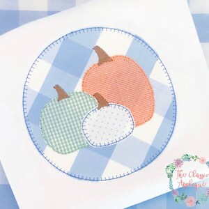 May include: A blue and white gingham fabric circle with three appliquéd pumpkins. The pumpkins are orange, green, and white with a white polka dot pattern.