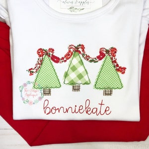 May include: White onesie with a red, green, and white applique of three Christmas trees with a red ribbon garland. The onesie has the name "bonniekate" embroidered in red below the applique.