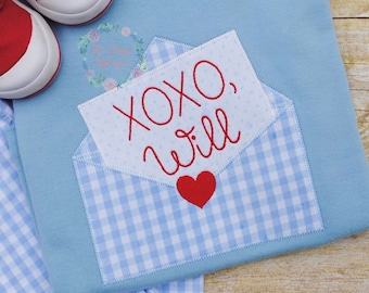 May include: A light blue baby onesie with a white and blue gingham envelope applique. The envelope has a red heart and the text "XOXO, Will" in red embroidery.