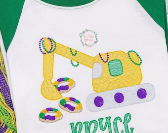 May include: White and green raglan shirt with a yellow excavator design, adorned with purple, green, and gold beads. The shirt features the name "Bryce" in green script, perfect for a child's wardrobe.
