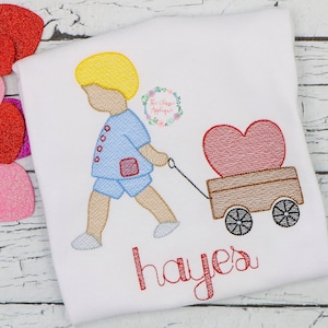 Peut inclure: Broderie représentant un garçon tirant un chariot avec un cœur rouge à l'intérieur. Le chariot a deux roues et le garçon porte un pantalon bleu et une chemise bleue. Le nom "Hayley" est brodé sous le dessin.