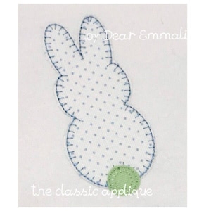 May include: A white fabric bunny applique with blue stitching and a green circle for a tail. The text "by Dear Emmali" and "the classic applique" are visible below the bunny.