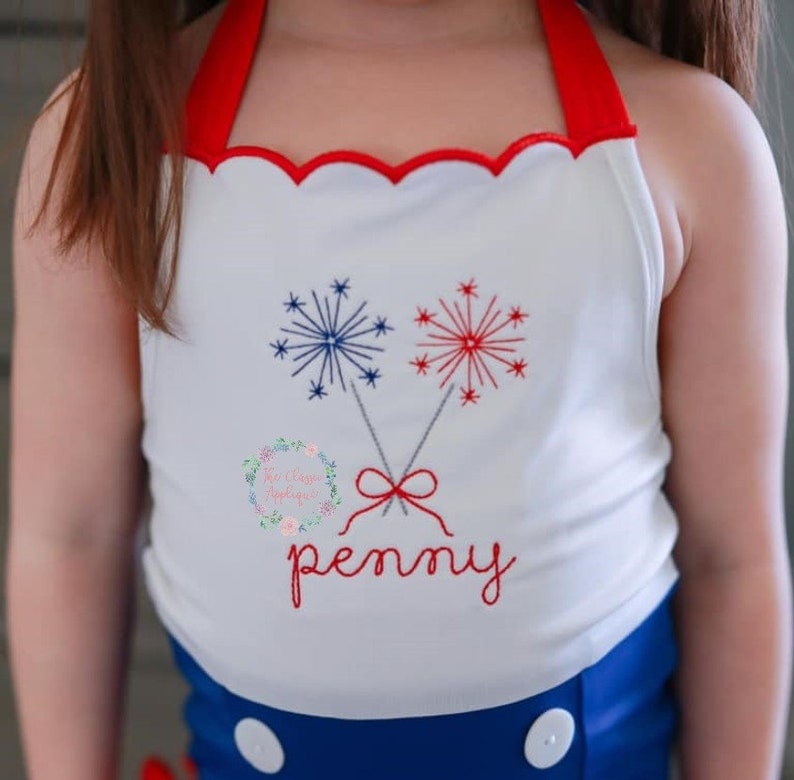 K&ouml;nnte beinhalten: Wei&szlig;es &auml;rmelloses Shirt mit rotem Besatz und einem gewellten Ausschnitt. Das Shirt zeigt ein gesticktes Design aus zwei roten und blauen Feuerwerksk&ouml;rpern mit einer roten Schleife und dem Namen "penny" darunter.