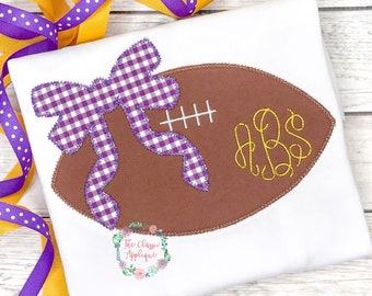 May include: Purple and white gingham bow on a brown football with yellow stitching and the monogram "ABS" in yellow thread.