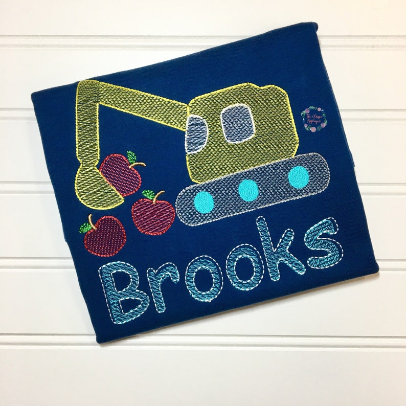May include: A blue t-shirt with an embroidered design of a yellow excavator digging up red apples. The name "Brooks" is embroidered below the excavator.
