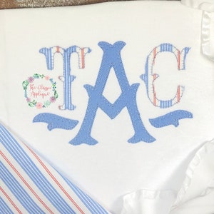 May include: A blue and white applique monogram of the letters "JAC" in a script font. The letters are stitched with a decorative stitch and have a vintage look.