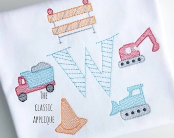 May include: A white embroidered applique with a blue and teal letter W surrounded by construction themed images. The images include a red dump truck, a blue bulldozer, a red excavator, a yellow traffic cone, and a gray construction barrier.