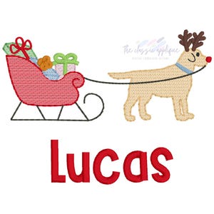 May include: An embroidered design featuring a tan dog with reindeer antlers pulling a red sleigh filled with wrapped gifts. The name "Lucas" is written in red below the sleigh and dog.