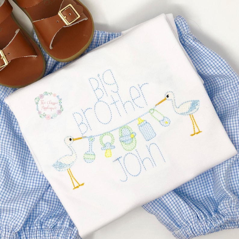 May include: White embroidered baby onesie with blue and white gingham fabric. The onesie says "Big Brother John" with two embroidered storks holding a string of baby items.
