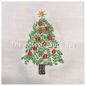 May include: A green embroidered Christmas tree applique with red ornaments and a gold star on top. The text "The classic applique" is below the tree.