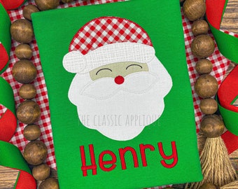 May include: Green Christmas shirt with a white Santa face applique with a red and white gingham hat. The name "Henry" is embroidered in red on the shirt.