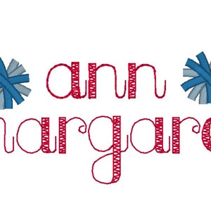 May include: Red embroidered text "ann margaret" with two blue and grey pom-poms on either side.