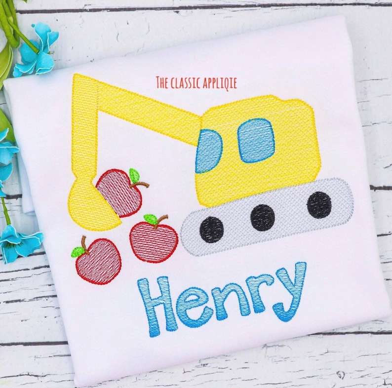 May include: An embroidered yellow excavator with a blue cab and black wheels is scooping up three red embroidered apples. The name "Henry" is embroidered in blue below the excavator.