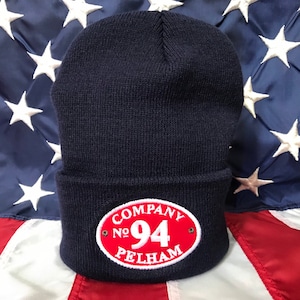 May include: A navy blue knit beanie with a red oval patch that says "COMPANY No. 94 PELHAM" in white lettering.