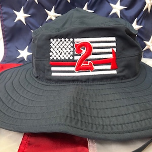 May include: A navy blue bucket hat with a red, white, and blue American flag patch. The patch features a red number "2" and a red axe. The hat has a thin red line across the flag.