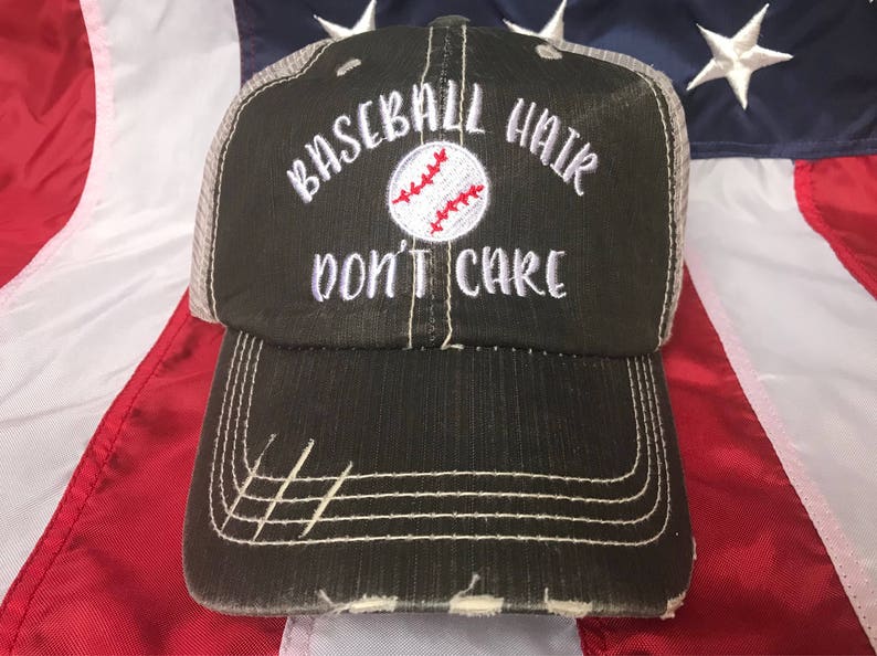 May include: A distressed black baseball cap with the text "BASEBALL HAIR DON'T CARE" embroidered in white. The baseball graphic is white with red stitching. The cap has a mesh back and a pre-curved bill.