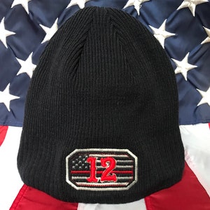 May include: Black knit beanie with a red and white American flag patch featuring the number 12.