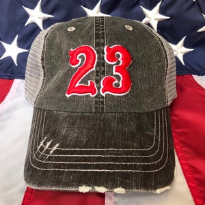 May include: A black and grey distressed trucker hat with a red embroidered number "23" on the front.