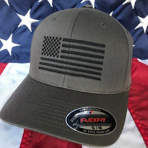 May include: A gray baseball cap with a black embroidered American flag on the front. The cap has a Flexfit label on the side with the text "The Original Flexfit S/M It Fits Your Life".