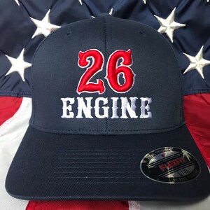 May include: A navy blue baseball cap with a red embroidered number "26" and white embroidered text "ENGINE". The cap has a Flexfit logo on the back.