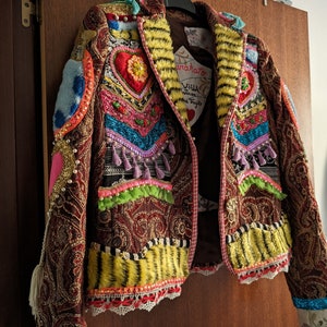 May include: A red, gold and black patterned jacket with colourful embellishments, including hearts, sequins and fringe. The jacket has a tiger print fur collar and a white lace trim.