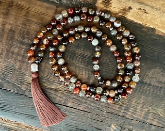 May include: A brown and white agate mala with a brown tassel. The mala has 108 beads and a silver charm.