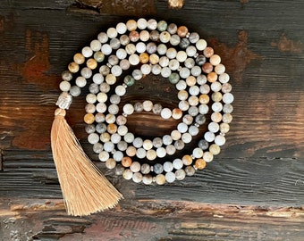 May include: A multi-colored stone mala necklace with a tassel. The beads are a mix of brown, white, and gray.