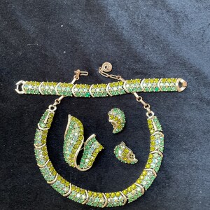 May include: A vintage green and yellow rhinestone jewelry set including a necklace, bracelet, and earrings. The set is made of gold-tone metal and features a leaf-shaped brooch.