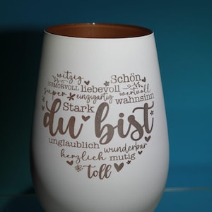 May include: White stemless wine glass with a brown rim. The glass features the German phrase "du bist" in a heart shape, surrounded by words like "beautiful" and "amazing".