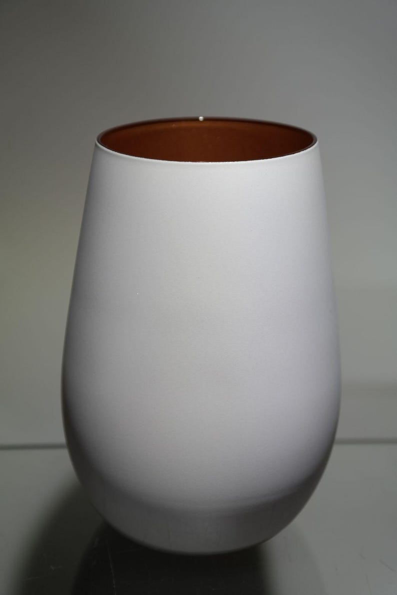 May include: A white, teardrop-shaped vase with a copper-colored interior. The vase has a smooth, matte finish and a wide opening. The design is simple and modern, suitable for home decor.