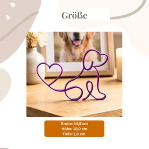 May include: A purple wire dog sculpture with a heart-shaped tail. The sculpture is on a wooden surface. The image also includes a framed photo of a dog, a vase with flowers, and a lit candle. The sculpture is 5.7 inches wide, 3.9 inches high, and 0.4 inches deep.
