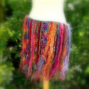 May include: A colourful crocheted skirt with long fringe in shades of pink, orange, purple, and blue.