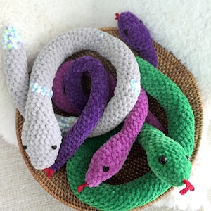 May include: Four crocheted snakes in a basket. The snakes are grey, purple, pink, and green.