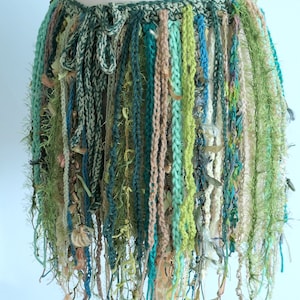 May include: A crocheted skirt with a green, blue and brown fringe. The skirt is made from a variety of yarns and textures.