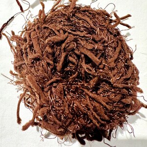 Peut inclure: Un &eacute;cheveau de fil brun avec une texture duveteuse. Le fil est compos&eacute; d'un m&eacute;lange de fibres, dont la laine et l'acrylique.