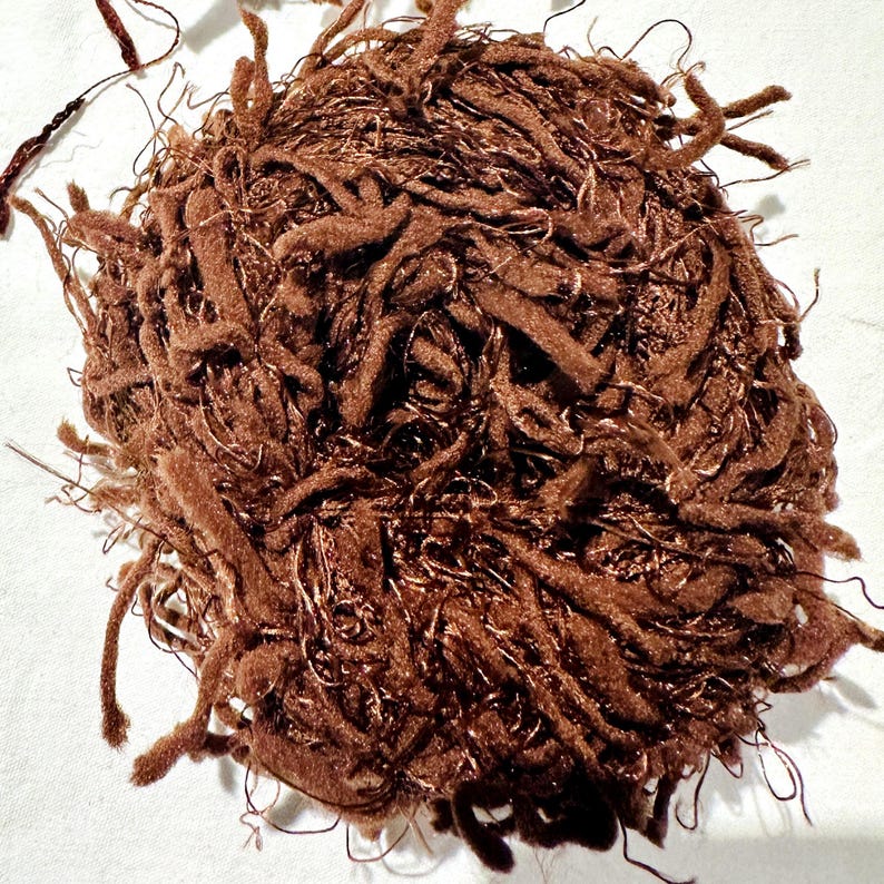Peut inclure: Un &eacute;cheveau de fil brun avec une texture duveteuse. Le fil est compos&eacute; d'un m&eacute;lange de fibres, dont la laine et l'acrylique.