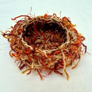 Peut inclure: Un petit panier rond en osier, tiss&eacute; &agrave; partir de fibres naturelles. Le panier est de couleur brun clair avec des accents rouges et orange. Le panier a un bord effiloch&eacute; et est parfait pour contenir de petits objets.